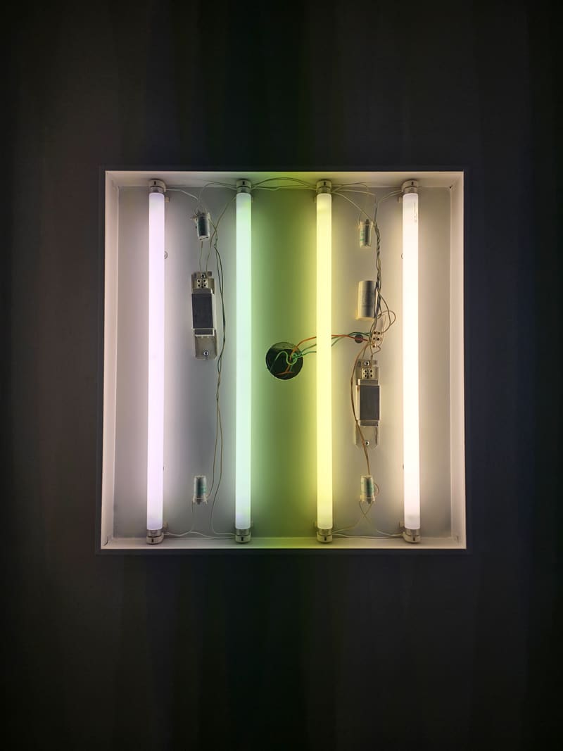 A wall light of four fluorescent tubes in pastel colours, glowing in the dark.