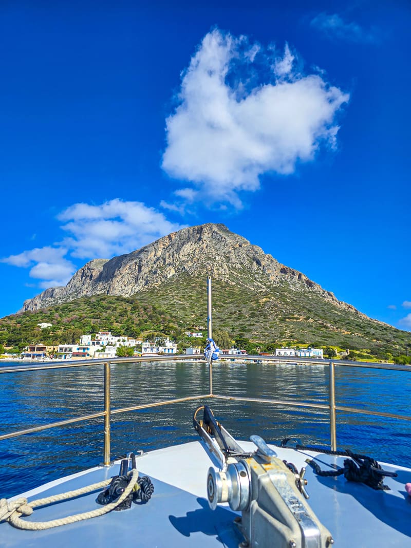 The bow of a boat heading toward a rocky mountain on the coast.
