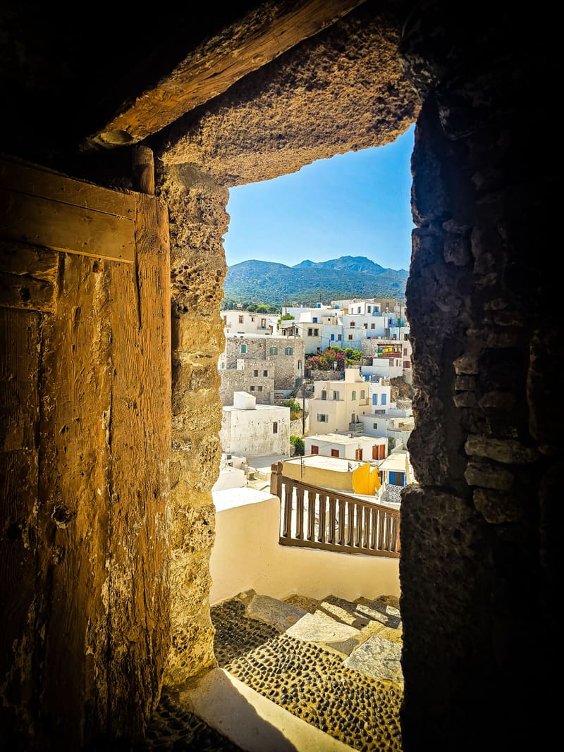 A dark stone doorway framing a sunlit view of white houses and hills.