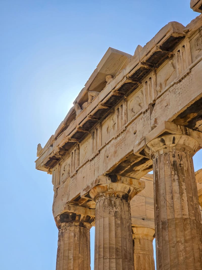 Looking up at the weathered columns and entablature of an ancient temple against blue sky.