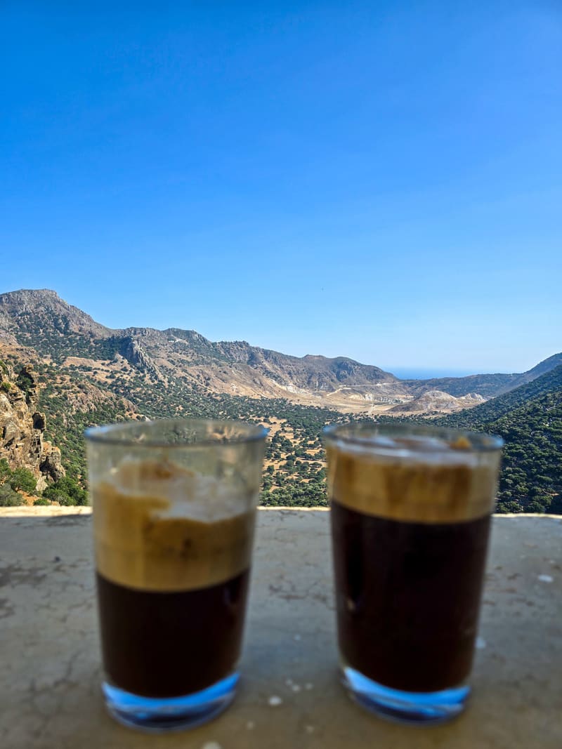 Two iced coffees on a ledge overlooking mountains.