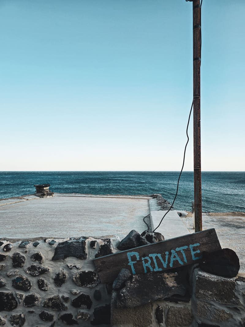 A rusty pole and a hand-painted "PRIVATE" sign by the sea.