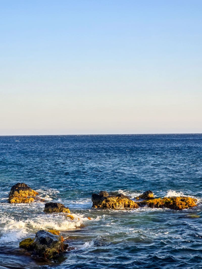 Waves washing over brown rocks in a blue sea.