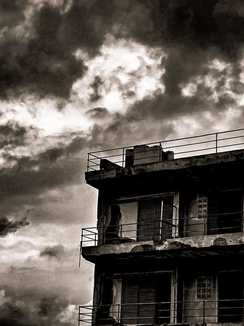 Black and white: the balconies of an abandoned concrete building under dramatic clouds.