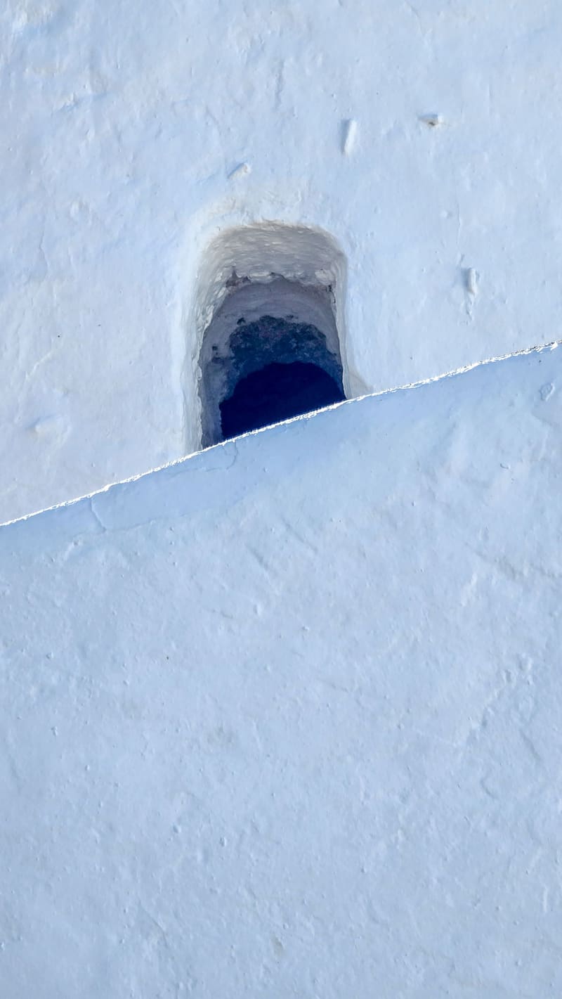 A small arched opening in a whitewashed wall, above a sloping white surface.