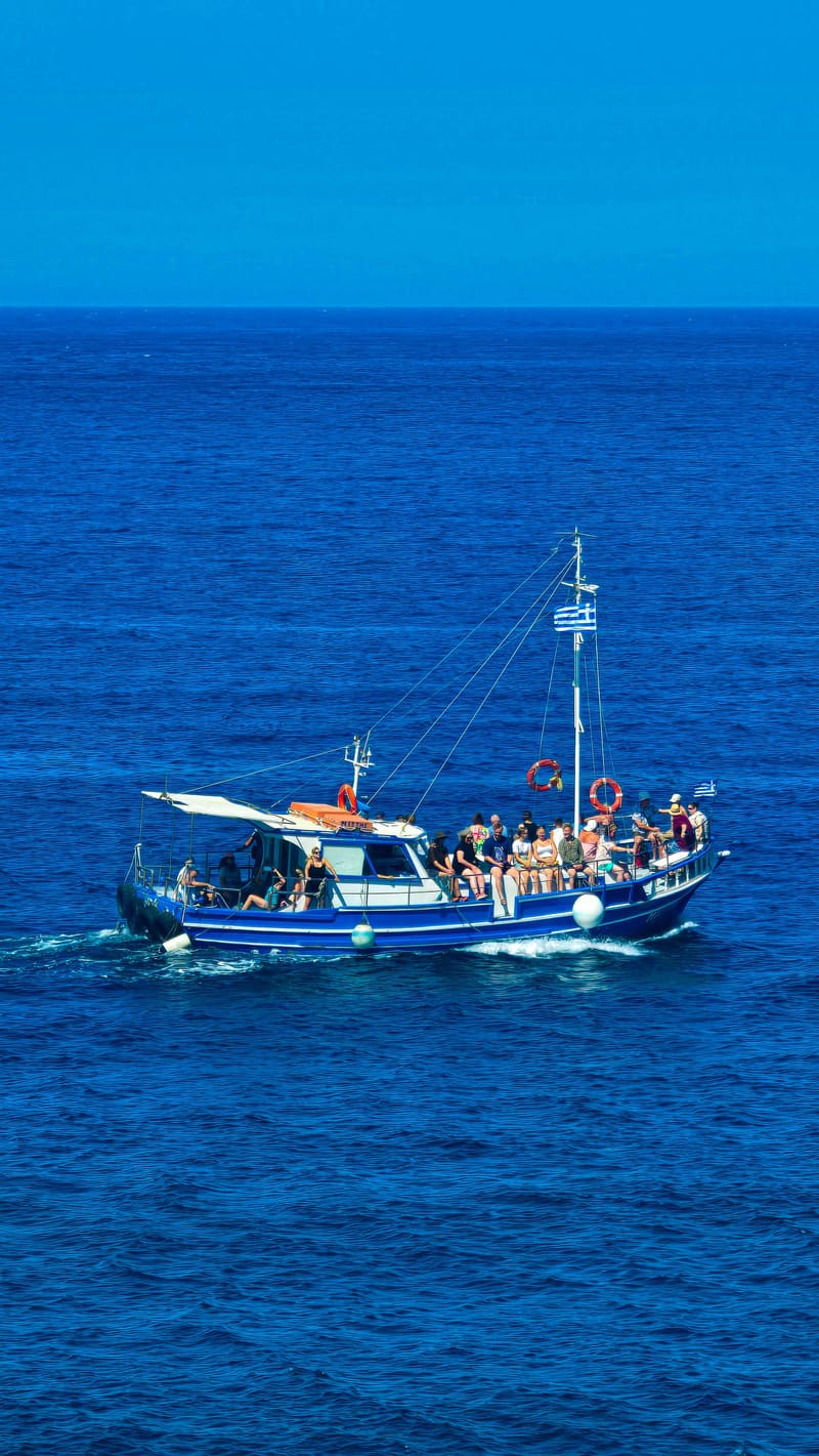 A blue fishing boat carrying passengers across a deep blue sea.