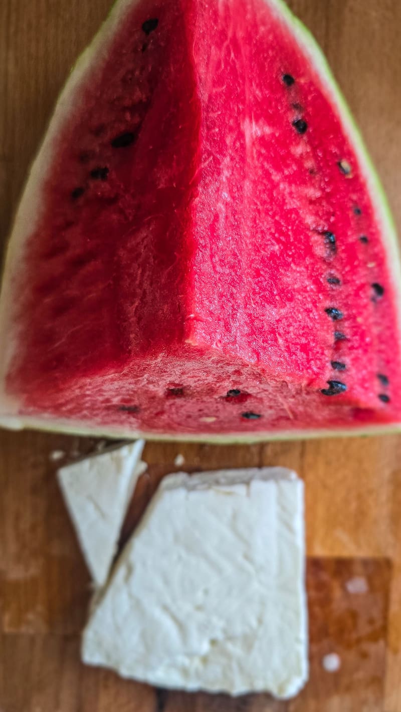 A wedge of watermelon and a block of feta on a wooden board.