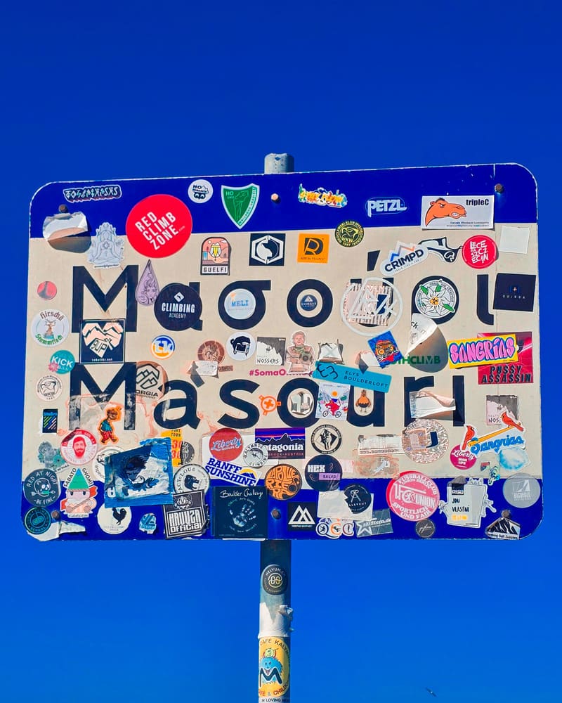 A road sign reading Masouri, covered in stickers, against a deep blue sky.