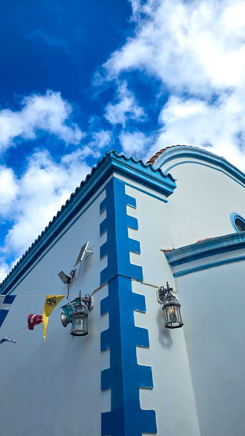 Looking up at a white and blue chapel wall with a lantern, under clouds.