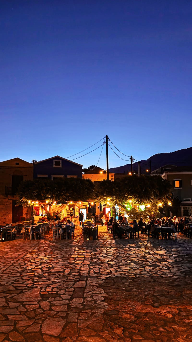 A lit taverna square at dusk.