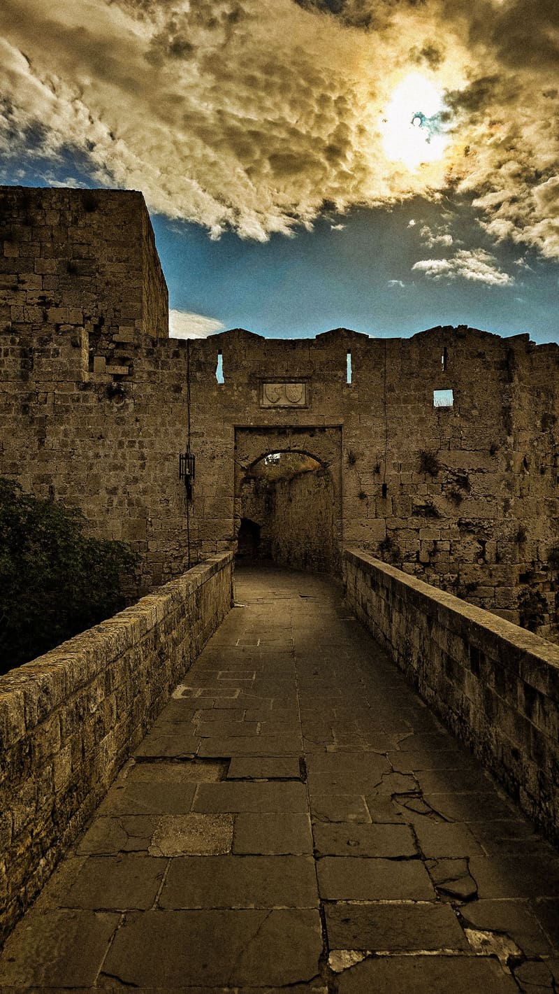 A stone castle passage under dramatic, sunlit clouds.